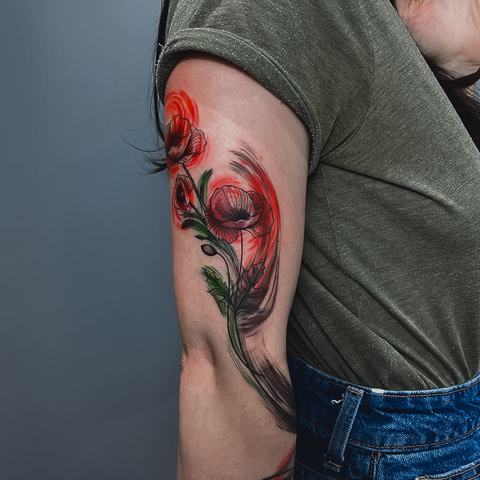 A bold upper-arm tattoo with a red and black portrait, flowing decorative elements and deep contrasting shading.