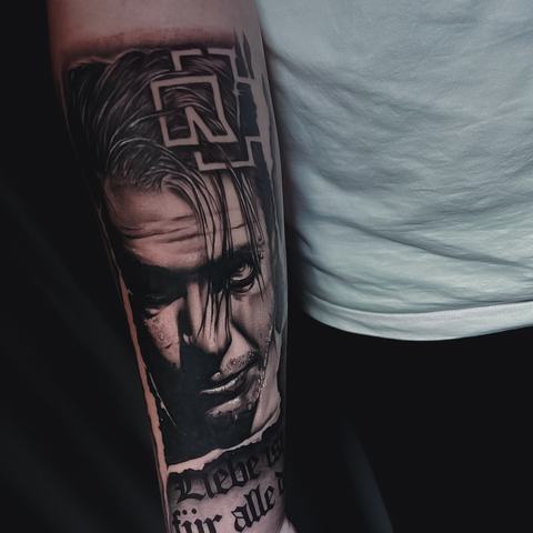 A black and grey forearm tattoo with a realistic portrait, bold geometric details and deep contrast.