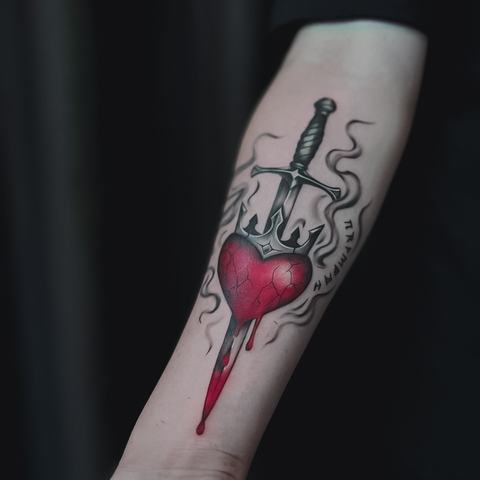 A red heart forearm tattoo with graphic black linework and a bold dripping effect.