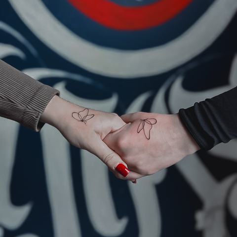 A pair of matching hand tattoos with delicate red details and fine minimalist linework.