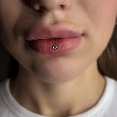 Lower lip piercing with minimalist jewellery that highlights the lip line and adds a clean, expressive detail to the overall look.