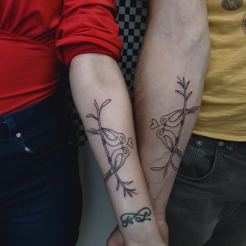 Matching forearm tattoos with delicate botanical linework, creating a subtle connected composition across both arms.
