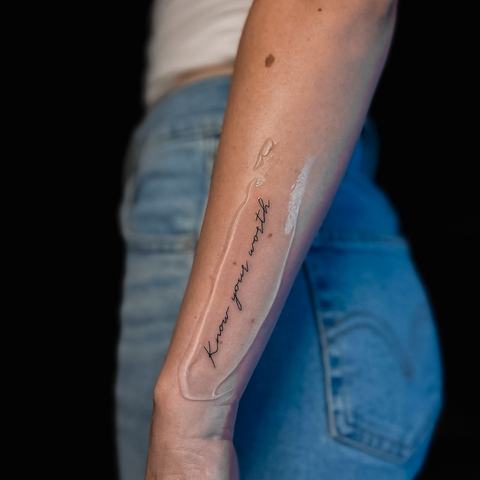A slender fine-line forearm tattoo with elongated abstract shapes, soft shading and a clean vertical flow.