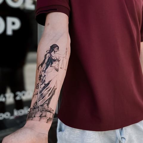 Grafisks tetovējums uz apakšdelma ar slaidu figūras motīvu, smalkām melnām līnijām un vertikāli izstieptu kompozīciju.