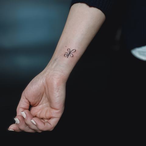 A tiny wrist tattoo with delicate linework and a subtle minimalist composition.