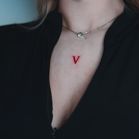 Минималистичная красная буква V в зоне декольте. Чистая геометричная форма и насыщенный оттенок делают небольшой рисунок заметным без лишних деталей.